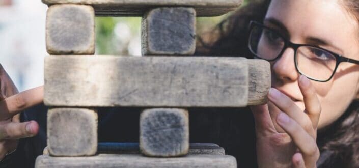 woman with eyeglasses trying to remove a jenga block from a jenga tower
