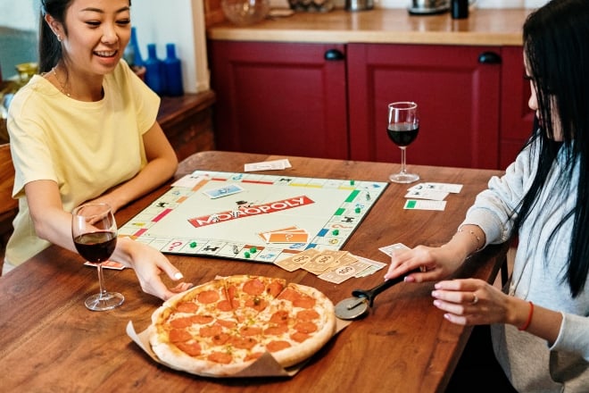 girls eating pizza while playing monopoly - party board games