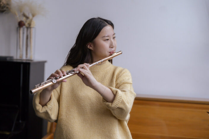 Girl in faded yellow sweatshirt playing a flute.