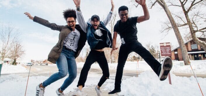 three men jumping on ground near bare trees